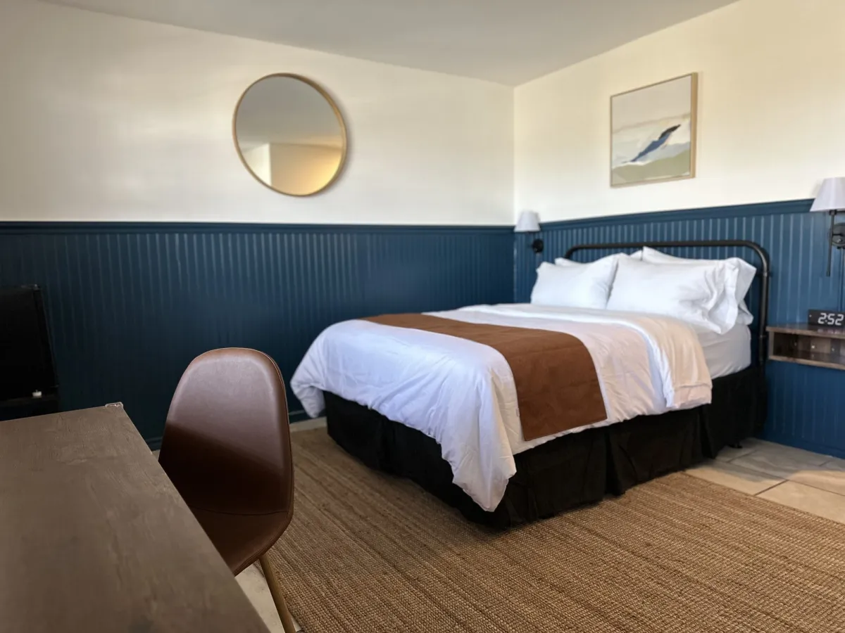 Queen room with navy beadboard, brass mirror and coastal art